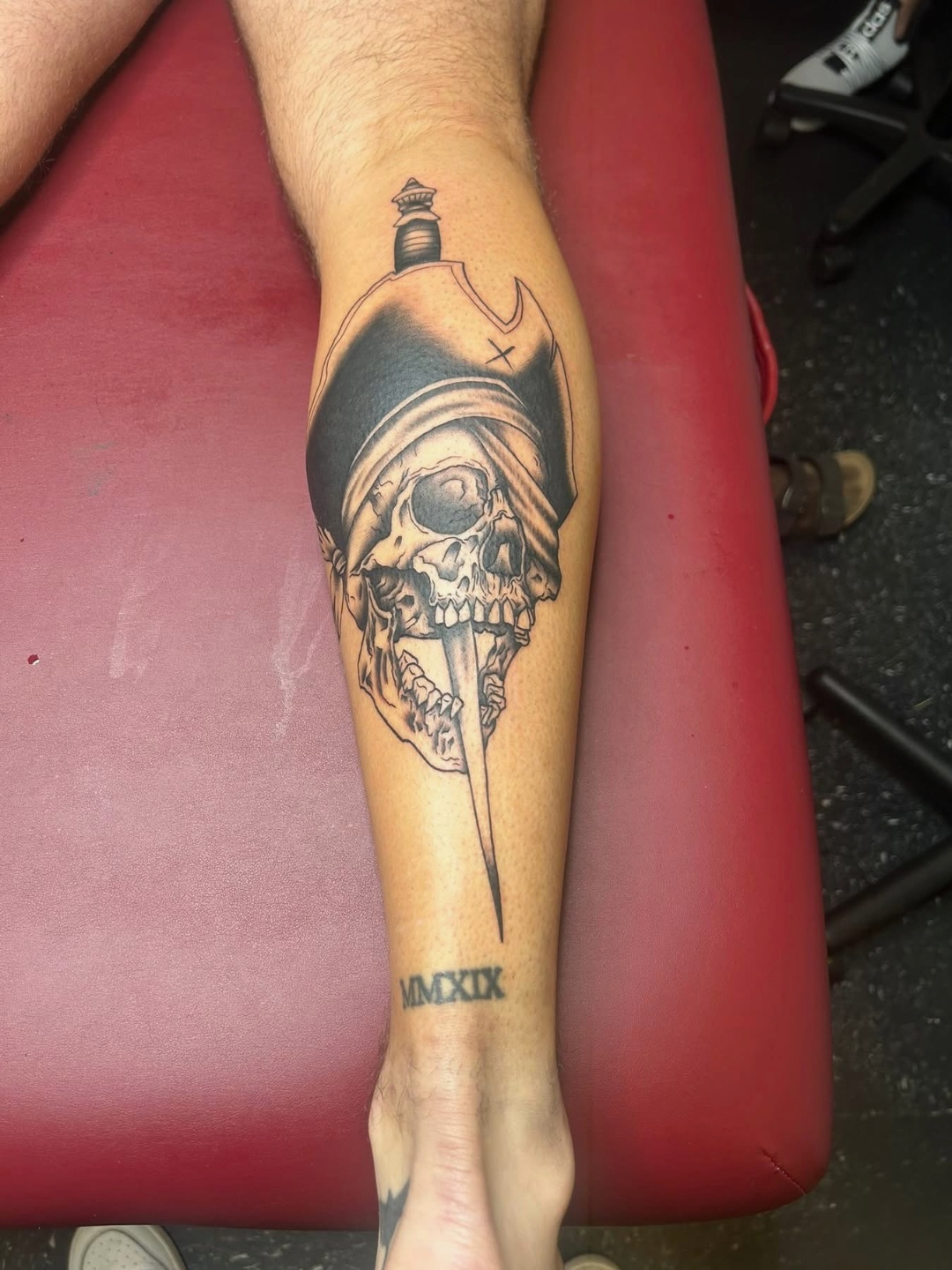 Black and grey pirate skull with dagger calf tattoo by CJ Upton