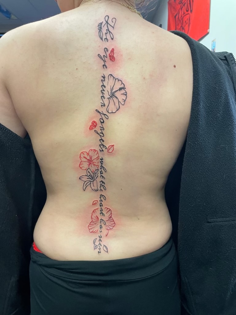 Spine script tattoo with red and black florals by Emma Bray